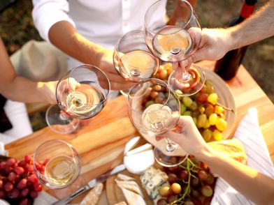 Weingläser stoßen über einem Tisch voller Trauben, Brot und Käse an, bei einem festlichen Treffen.