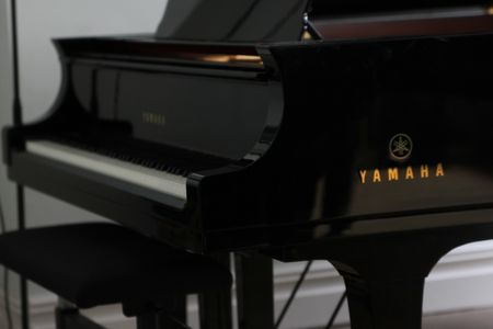 Ein schwarzer Flügel der Marke Yamaha steht in einem lichtdurchfluteten Raum neben einem Hocker.
